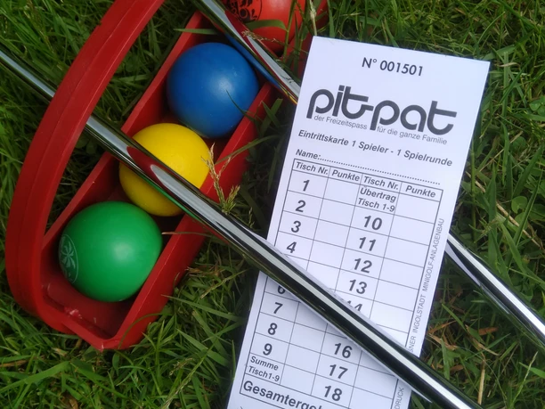 PitPat Hümmlinger Land Bunte PitPat-Bälle und Schläger liegen auf Gras neben einer Spielkarte mit Punkten und Spielfeldnummern.