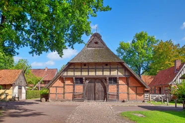 ammerlaender-bauernhaus Historisches Ammerländer Bauernhaus mit Reetdach, Fachwerk und großen Holztoren im Sonnenlicht.