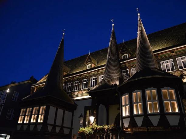Altes Rathaus bei Nacht Beleuchtetes Fachwerkgebäude mit drei spitzen Türmen vor dunkelblauem Nachthimmel in Einbeck.