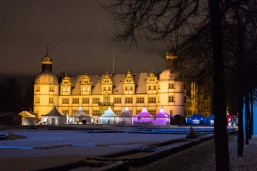 Beleuchtetes Schloss im Winter, umgeben von festlich beleuchteten Marktständen im Hintergrund.