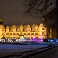 Weihnachtszauber Schloß Neuhaus Beleuchtetes Schloss im Winter, umgeben von festlich beleuchteten Marktständen im Hintergrund.