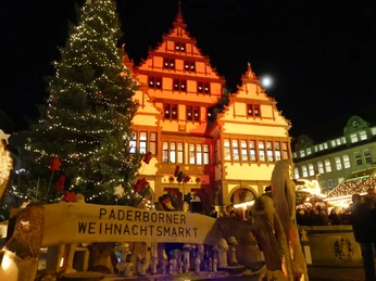 Marktstände und ein beleuchteter Tannenbaum vor einem historischen Gebäude am Paderborner Weihnachtsmarkt.