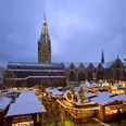 Weihnachtsmarkt auf dem Domplatz mit schneebedeckten Ständen, Lichtern und einer Kirche im Hintergrund.