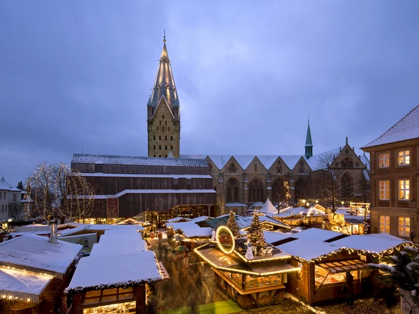 Weihnachtsmarkt auf dem Domplatz mit schneebedeckten Ständen, Lichtern und einer Kirche im Hintergrund.