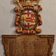 Wappen an der Kirche St. Johannes Baptist_HRenerig.jpg Wappenrelief mit historischer Inschrift, verziert mit Kronen und Wappenmotiven, an der Kirchenwand.