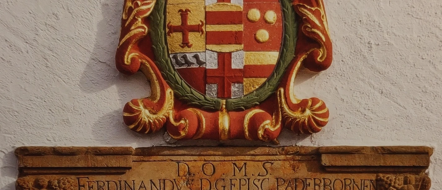 Wappen an der Kirche St. Johannes Baptist_HRenerig.jpg Wappenrelief mit historischer Inschrift, verziert mit Kronen und Wappenmotiven, an der Kirchenwand.
