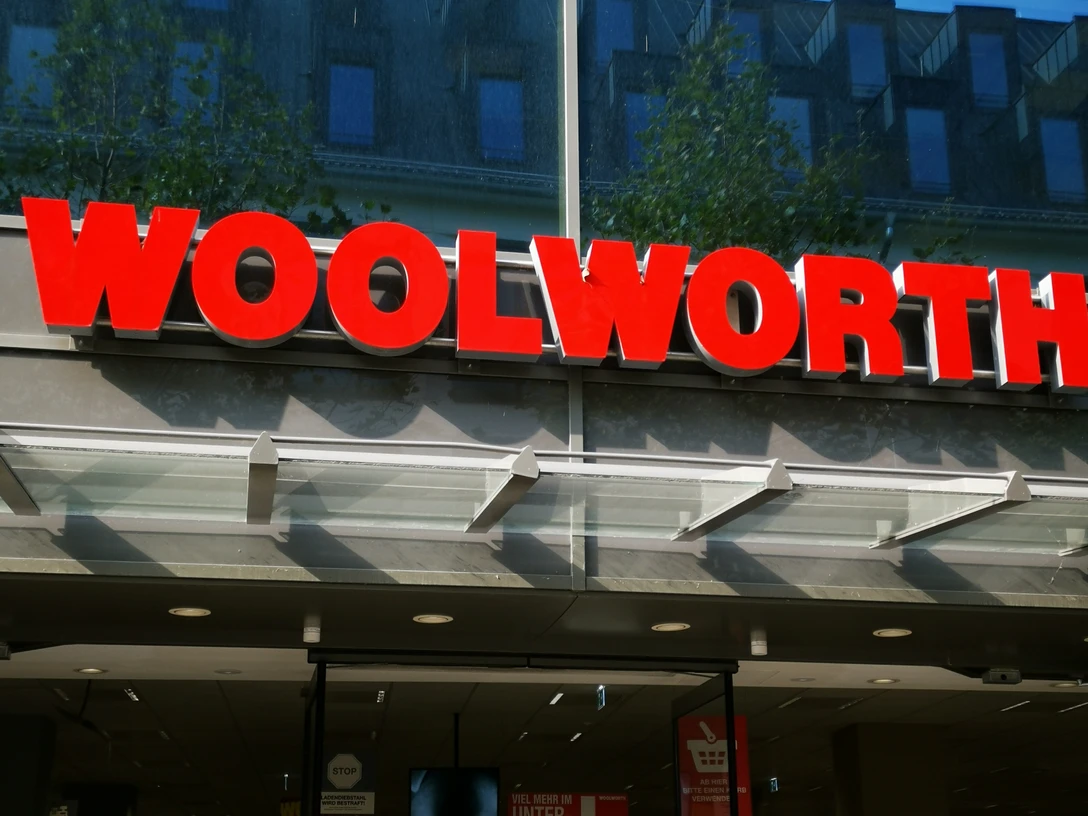 Das Bild zeigt das Schild "Woolworth" über dem Eingang des Geschäftes.