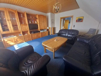 Wohnzimmer Helles Wohnzimmer mit Holzmöbeln, dunklen Ledersofas und einem blauen Teppichboden.