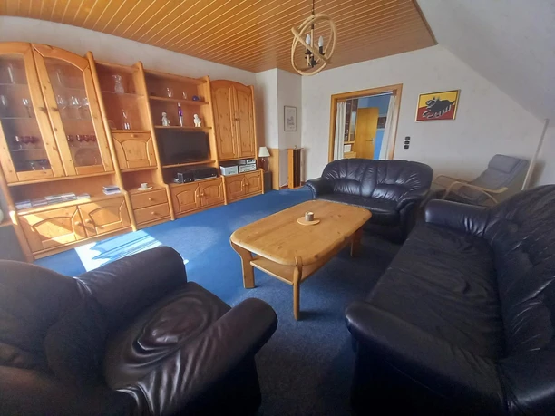 Wohnzimmer Helles Wohnzimmer mit Holzmöbeln, dunklen Ledersofas und einem blauen Teppichboden.