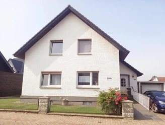 Haus vorne Ein weißes Einfamilienhaus mit kiesbedecktem Schrägdach und Vorgarten, eingebettet in eine ruhige Wohngegend.