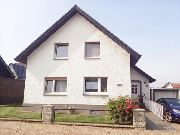 Haus vorne Ein weißes Einfamilienhaus mit kiesbedecktem Schrägdach und Vorgarten, eingebettet in eine ruhige Wohngegend.