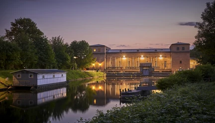 Wasserkraftwerk Raffelberg, Mülheim an der Ruhr Wasserkraftwerk Raffelberg in der Abenddämmerung, umgeben von Wasser und üppigem Grün.
