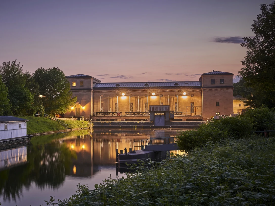 Wasserkraftwerk Raffelberg, Mülheim an der Ruhr Wasserkraftwerk Raffelberg in der Abenddämmerung, umgeben von Wasser und üppigem Grün.