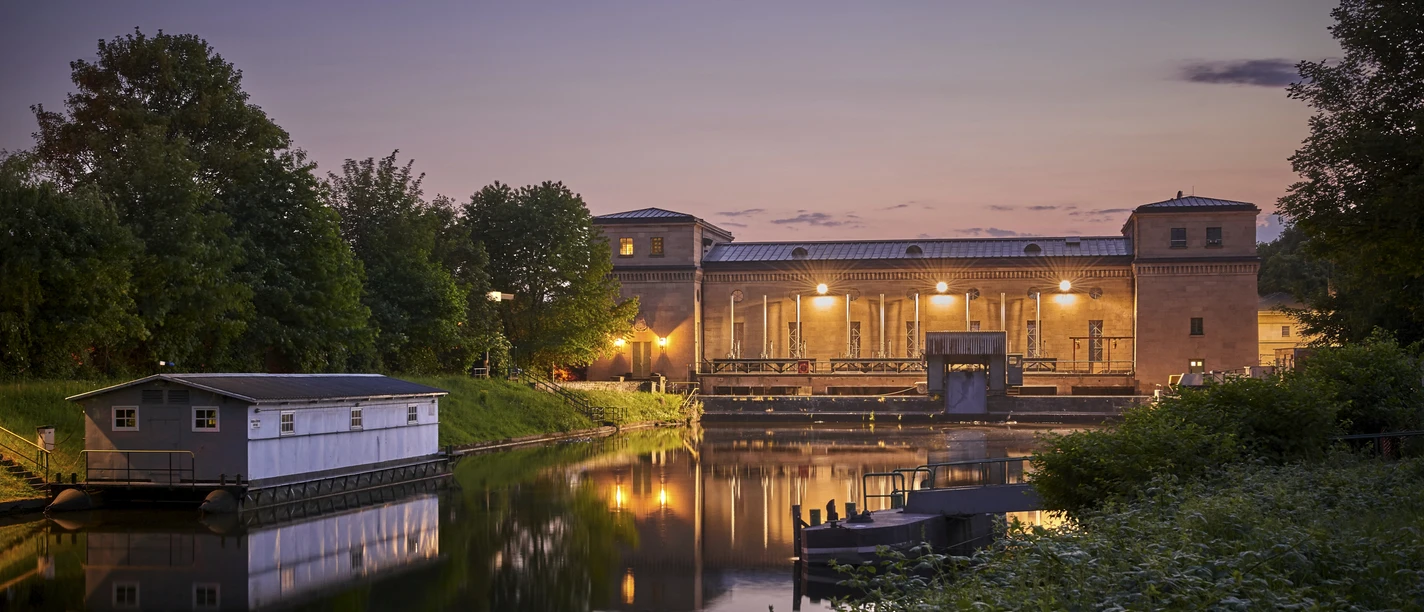 Wasserkraftwerk Raffelberg, Mülheim an der Ruhr Wasserkraftwerk Raffelberg in der Abenddämmerung, umgeben von Wasser und üppigem Grün.