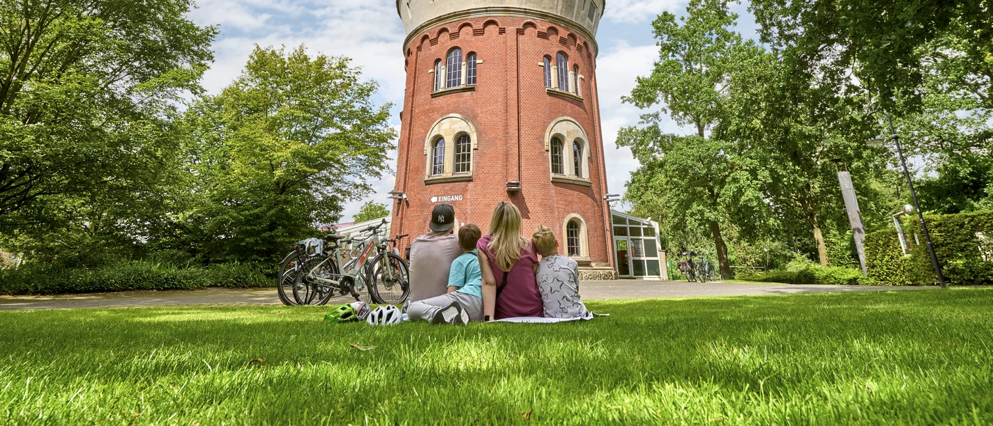Familie entspannt auf einer Wiese vor dem runden Turm der Camera Obscura in Mülheim an der Ruhr.