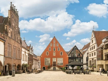 Historische Altstadt mit Kopfsteinpflaster, umgeben von gotischen und modernen Gebäuden unter blauem Himmel.