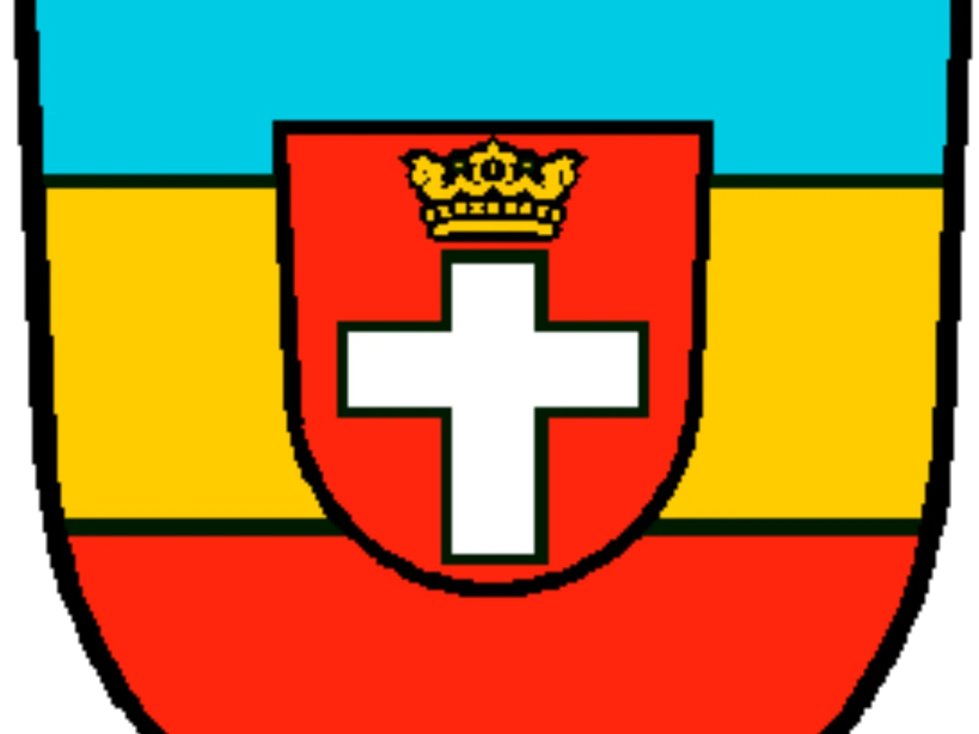 Wappen.png Wappen in Blau, Gelb und Rot mit weißem Kreuz in der Mitte und einer Krone darüber.