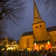 Menschen genießen den stimmungsvollen Adventsmarkt vor einer beleuchteten Kirche in der Dämmerung.