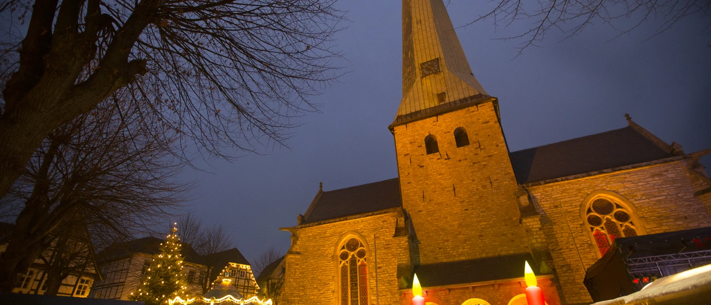 Menschen genießen den stimmungsvollen Adventsmarkt vor einer beleuchteten Kirche in der Dämmerung.