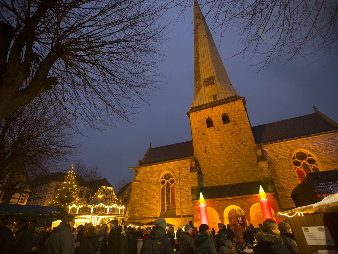 Delbrücker Adventsmarkt Menschen genießen den stimmungsvollen Adventsmarkt vor einer beleuchteten Kirche in der Dämmerung.