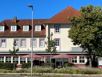 Een traditioneel gebouw met een zadeldak en verschillende ramen, geflankeerd door hoge bomen.