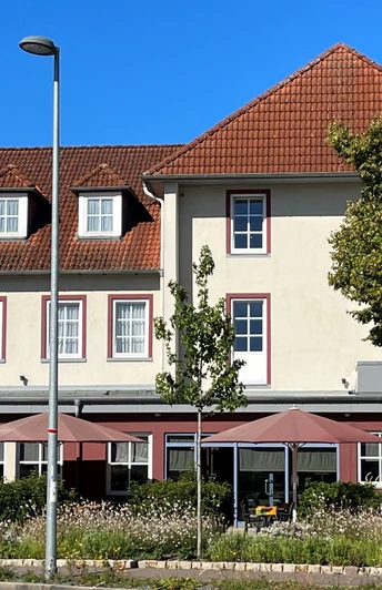 Ein traditionelles Gebäude mit Satteldach und mehreren Fenstern, flankiert von hohen Bäumen.