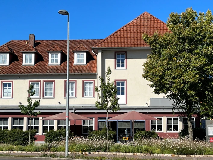 Gieschens Hotel Ein traditionelles Gebäude mit Satteldach und mehreren Fenstern, flankiert von hohen Bäumen.