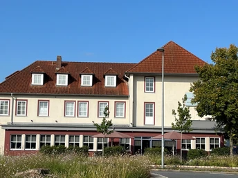 Gieschens Hotel mit rotem Ziegeldach und weißen Fensterrahmen vor blauem Himmel in grüner Umgebung.