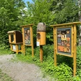Bienenlehrpfad in Erkrath Drei hölzerne Informationstafeln und Bienenbehausungen stehen inmitten einer grünen Landschaft.