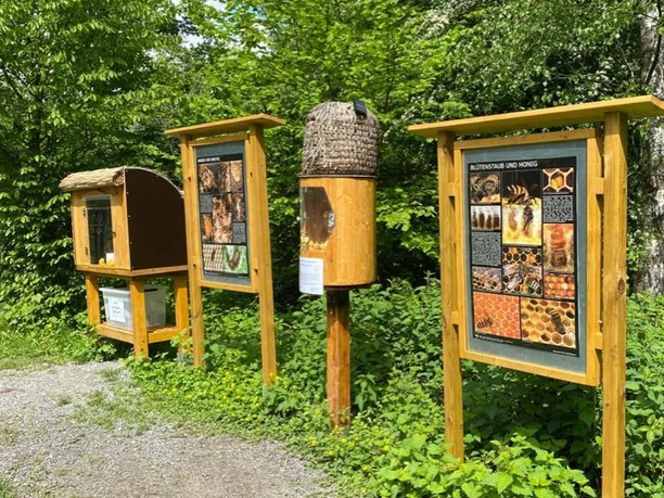 Bienenlehrpfad in Erkrath Drei hölzerne Informationstafeln und Bienenbehausungen stehen inmitten einer grünen Landschaft.
