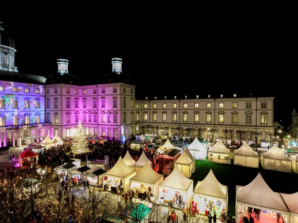 Unikat Weihnachtsmarkt Nächtlicher Weihnachtsmarkt vor einem historischen Gebäude mit erleuchteten Fassaden und festlichen Ständen.
