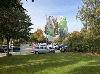Golf Park Steinhuder Meer Drei Fahnen wehen vor einem Parkplatz mit Autos, umgeben von herbstlichen Bäumen und grünem Rasen.Three flags fly in front of a parking lot with cars, surrounded by autumnal trees and green lawns.Tre flag vajer foran en parkeringsplads fuld af biler, omgivet af efterårstræer og grønne plæner.Drie vlaggen wapperen voor een parkeerplaats vol auto's, omringd door herfstige bomen en groene gazons.
