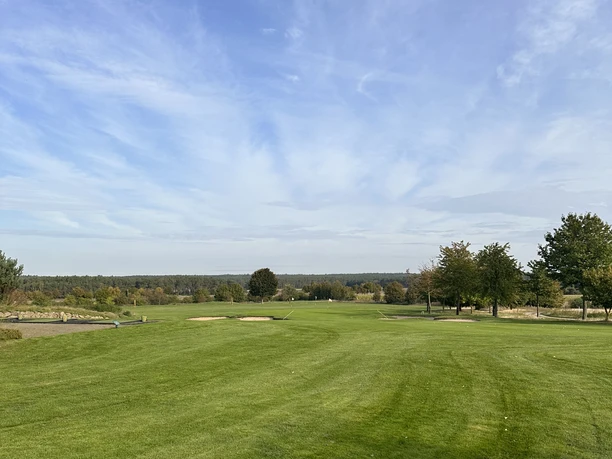 Extensive golf meadow with a deep blue sky, surrounded by scattered trees on the horizon.