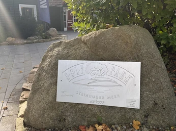 Golf Park Steinhuder Meer Ein großer Stein mit gravierter Metallplatte "Golf Park Steinhuder Meer", umgeben von Laub und Pflanzen.A large stone with engraved metal plate "Golf Park Steinhuder Meer", surrounded by foliage and plants.En stor sten med indgraveret metalplade "Golf Park Steinhuder Meer", omgivet af blade og planter.Een grote steen met een gegraveerde metalen plaat "Golfpark Steinhuder Meer", omringd door gebladerte en planten.