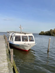 Fahrgastschiff Willkommen Fahrgastschiff an einem Steg im Wasser, ruhige Umgebung, leichter Wellengang unter blauem Himmel.
