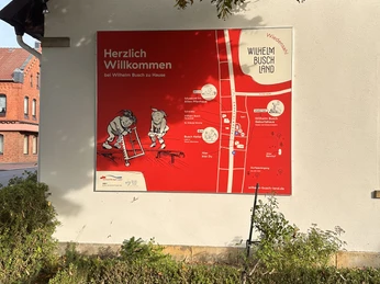 Wilhelm Busch Land Wiedensahl Eine leuchtend rote Infotafel am Wilhelm Busch Land weist auf kulturelle Attraktionen hin.A bright red information board at Wilhelm Busch Land points out cultural attractions.En knaldrød informationstavle i Wilhelm Busch Land viser vej til kulturelle attraktioner.Een felrood informatiebord in Wilhelm Busch Land wijst op culturele attracties.