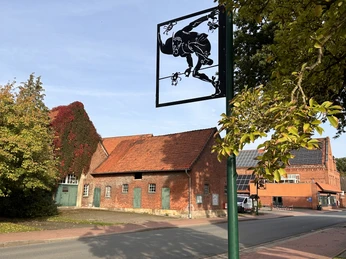 Wilhelm Busch Land Wiedensahl Ein unscheinbares Dorfhaus unter blauem Himmel, verziert mit einem Busch'schem Metallschild.An inconspicuous village house under a blue sky, decorated with a Busch metal sign.Et uanseligt landsbyhus under en blå himmel, dekoreret med et Busch-metalskilt.Een onopvallend dorpshuis onder een blauwe hemel, versierd met een metalen bord van Busch.