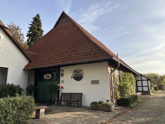 Historisches, rotes Backsteinhaus mit Satteldach, umgeben von grünem Garten, mit Eingangstür.