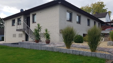 Ferienwohnung in modernem Bungalow aus weißem Ziegel mit gepflegtem Weg, Pflanzen und Rasen.