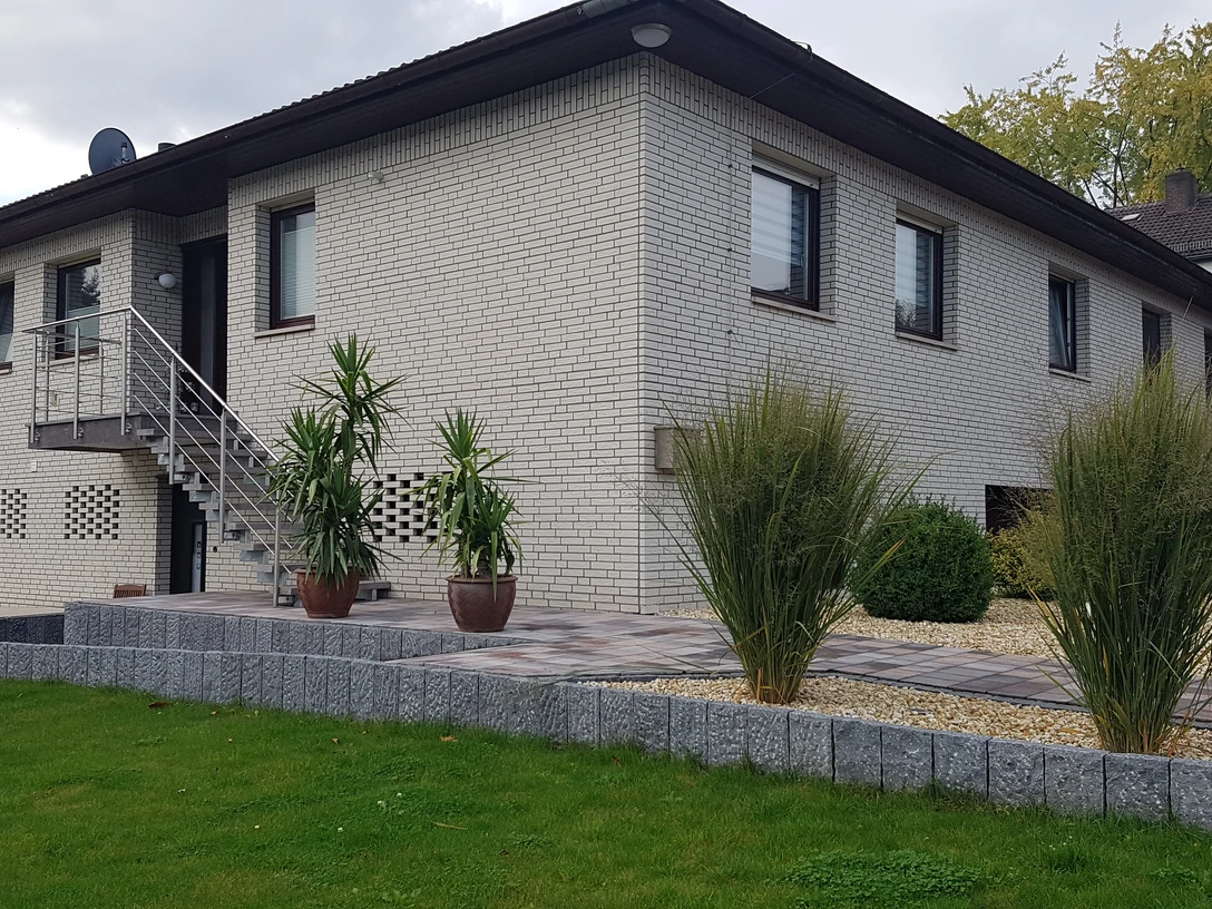 Ferienwohnung in modernem Bungalow aus weißem Ziegel mit gepflegtem Weg, Pflanzen und Rasen.