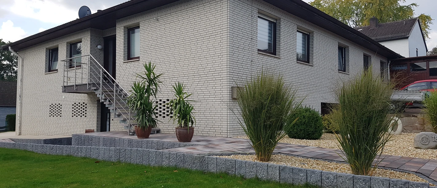 Ferienwohnung in modernem Bungalow aus weißem Ziegel mit gepflegtem Weg, Pflanzen und Rasen.