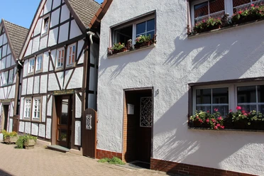 Fachwerkhäuser mit farbenfrohen Fensterblumen und gepflastertem Gehweg unter sonnigem Himmel.