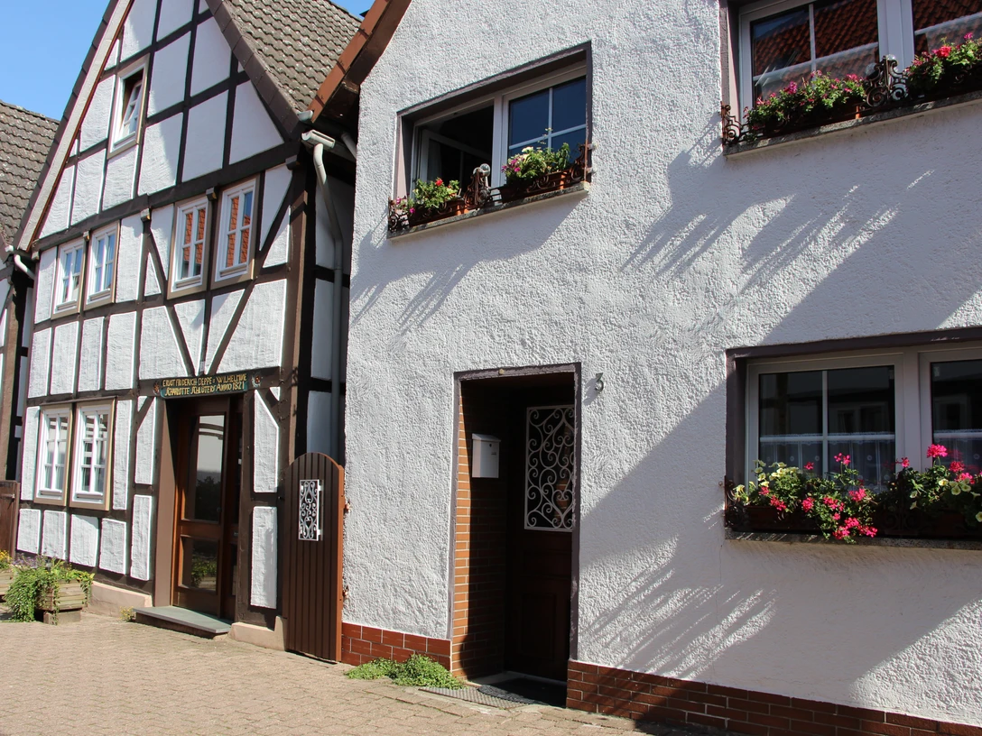 Fachwerkhäuser mit farbenfrohen Fensterblumen und gepflastertem Gehweg unter sonnigem Himmel.