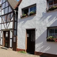 Fachwerkhäuser mit farbenfrohen Fensterblumen und gepflastertem Gehweg unter sonnigem Himmel.