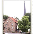 Ferienwohnung Capella.gif Ein Backsteinhaus mit grünem Baum im Vordergrund, dahinter ein Kirchturm in ländlicher Umgebung.