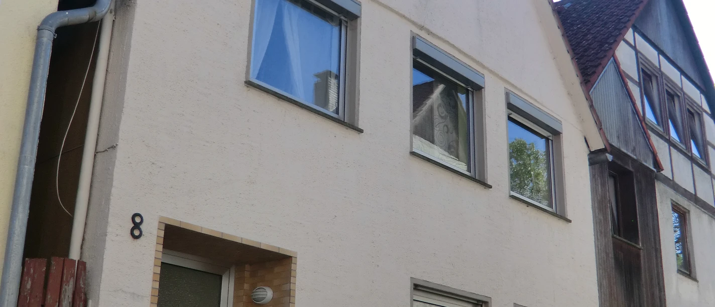 Ferienhaus mit hellem Putz, drei Etagen und großen Fenstern, steht in einer ruhigen Straße.