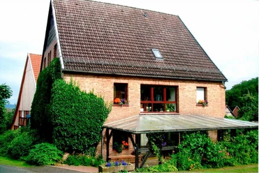 Ein Ziegelbau mit Satteldach, umgeben von grüner Vegetation, bietet Pflanzendekor an Fenstern und Terrasse.