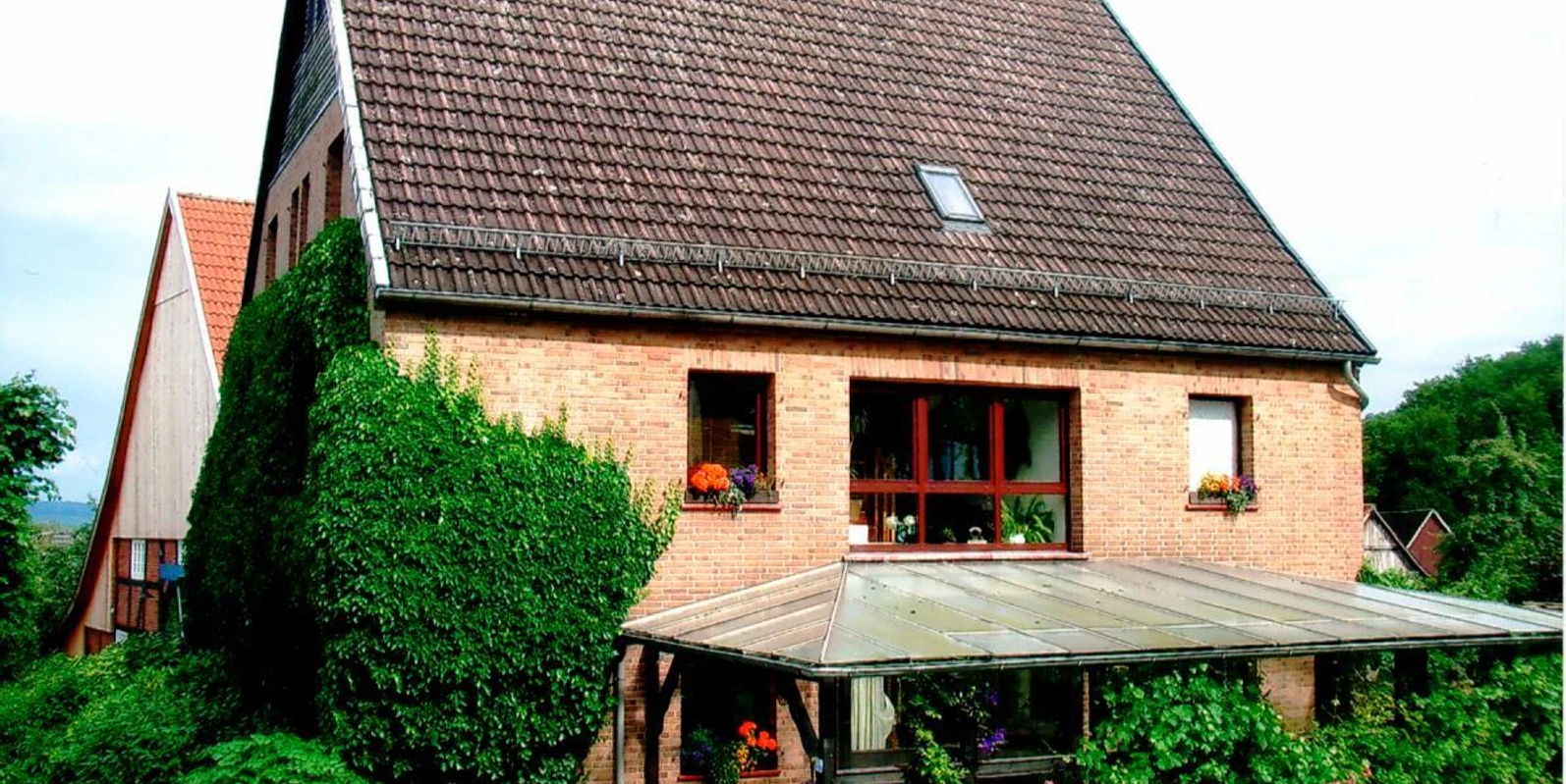 Ein Ziegelbau mit Satteldach, umgeben von grüner Vegetation, bietet Pflanzendekor an Fenstern und Terrasse.