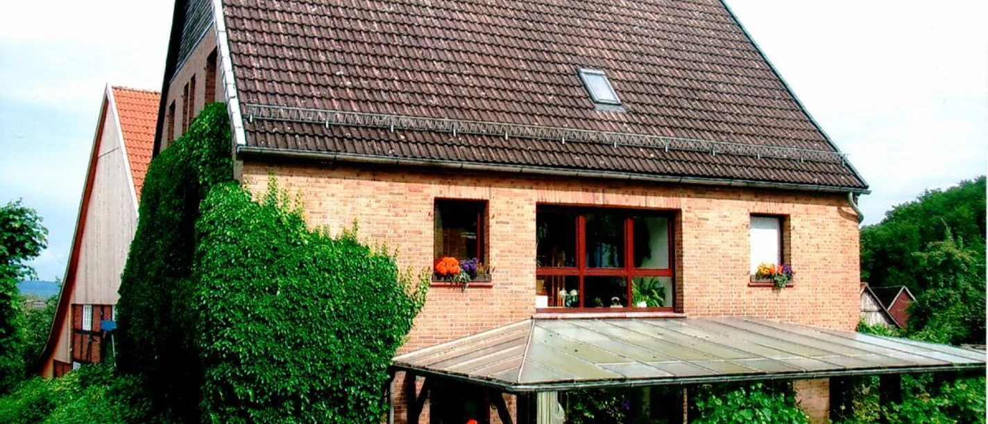 Ferienwohnung Merkord.JPG Ein Ziegelbau mit Satteldach, umgeben von grüner Vegetation, bietet Pflanzendekor an Fenstern und Terrasse.