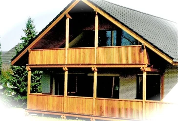 Ferienwohnung Rautenberg_Foto.jpg Zweistöckiges Haus mit großen Holzbalkonen und schrägem Dach, umgeben von Nadelbäumen.